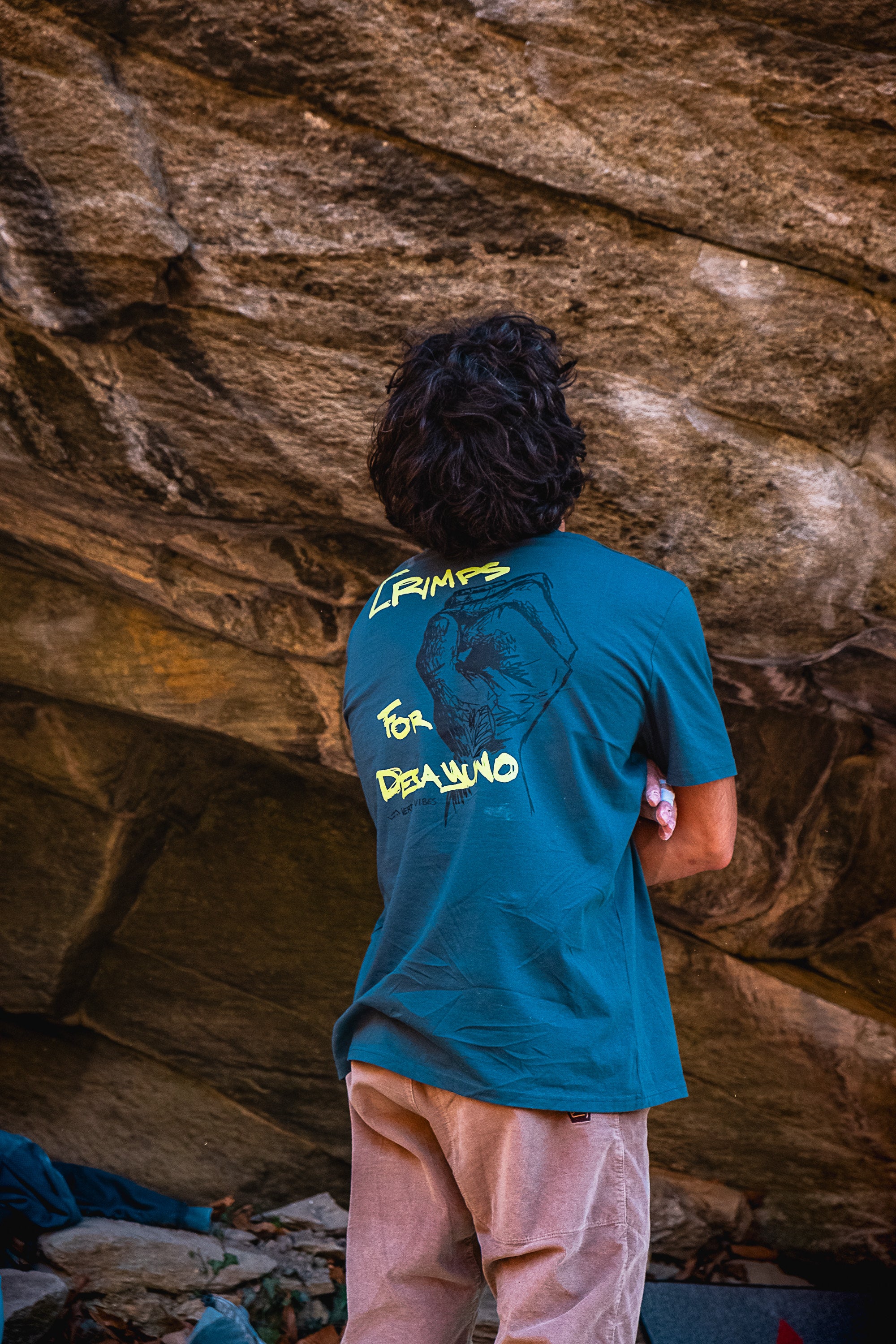 Person wearing a blue crimps for desayuno t-shirt from vertical vibes, standing in front of a rocky wall.