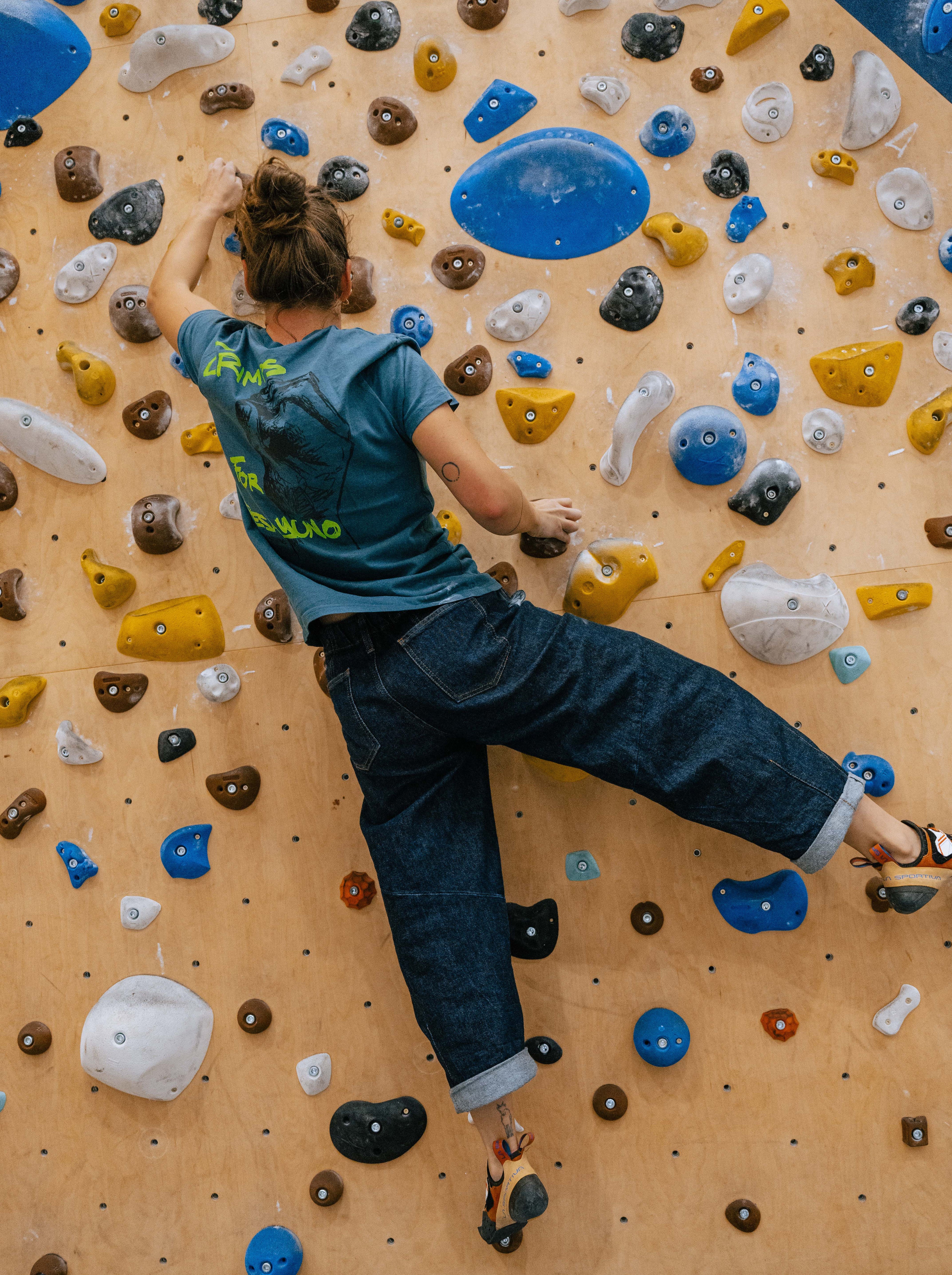 Person climbing in a climbing gym with blue crimps for desayuno t-shirt from vertical vibes