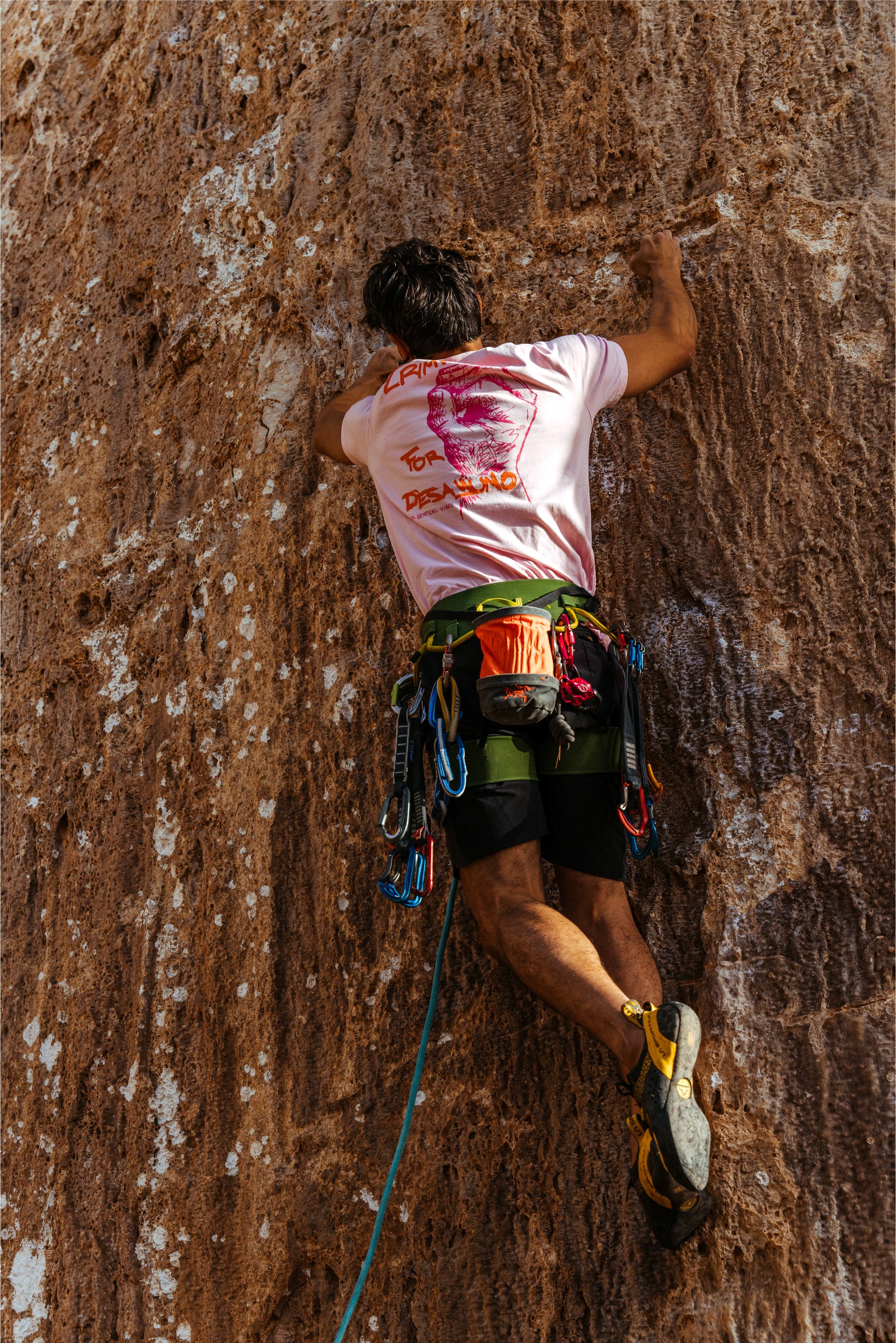 Person rock climbing and wearing a pink crimps for desayuno t-shirt by vertical vibes